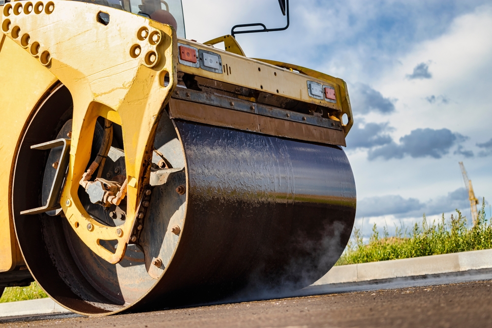Vibratory road roller lays asphalt on a new road under construction. Close-up of the work of road machinery. Construction work on the construction of urban highways